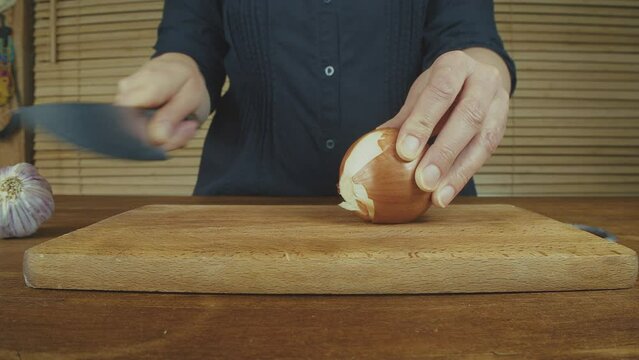 Woman's hands close up cutting onion and smashing, and peeling garlic on a wooden board with a big knife. Wooden kitchen table. . High quality 4k footage