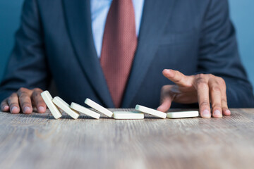 Business man stoping domino effect by his hand, business strategy background image, wearing blue...