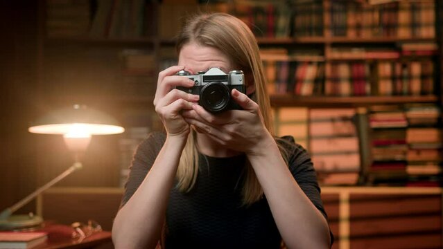 attractive young woman in retro clothes in a vintage room takes pictures with an old camera. A girl with blond hair, a professional photographer takes pictures. After photo she nods her head