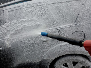 From a special gun at the car wash, white foam is applied to the car for chemical cleaning of the...