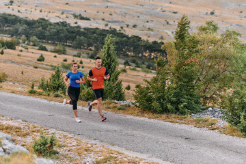 A couple dressed in sportswear runs along a scenic road during an early morning workout, enjoying...