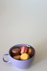 Purple cup filled with pastel macarons on white background. Selective focus.