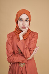 Beautiful female model wearing classic orange color kebaya with hijab, an Asian traditional dress for Muslim woman isolated over beige background. Eidul fitri festival fashion and beauty concept.