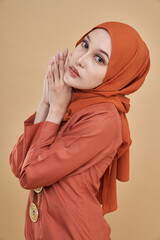 Beautiful female model wearing classic orange color kebaya with hijab, an Asian traditional dress for Muslim woman isolated over beige background. Eidul fitri festival fashion and beauty concept.