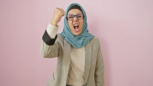 Furious middle-aged hispanic woman in hijab, fists clenched in a display of raw anger, shouting in pure rage! in a world painted pink, her frustration echoes in the isolated background.