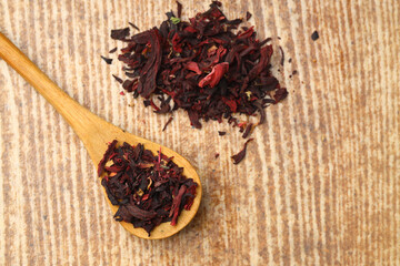 Karkade tea. Hibiscus tea leaves in wooden spoon isolated on wooden background. File contains clipping path. Top view. Selective focus.