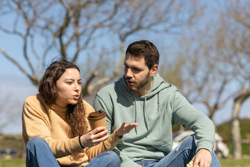 couple argue while talking in the park drinking coffee