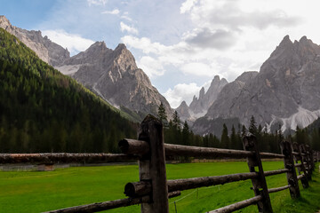 Scenic hiking trail along alpine meadow secured by wooden fence in panoramic valley Fischleintal...