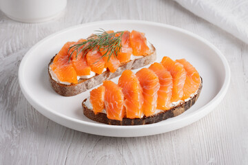 Rye sandwich with salmon and cream cheese on white wooden table