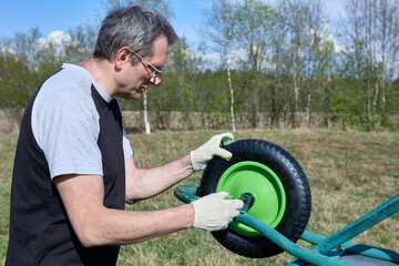 Repair of garden wheelbarrow in open air, gardener changes wheel.