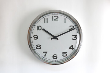 A round shape stainless steel wall clock with white face and hands set to 10:10 o'clock time. The clock is hanging on a wall.