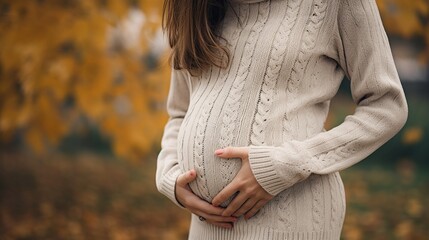 a Close up of pregnant woman in sweater touching her belly in the autumn park.
