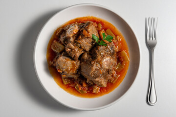 Isolated Bowl with a portion of oxtail stewed vaccinara and fork