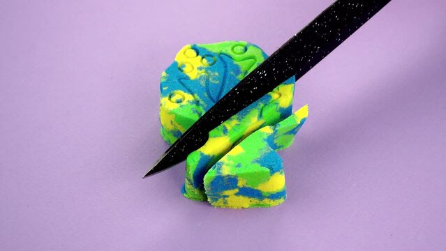 Very Satisfying and Relaxing Kinetic Sand ASMR. Cutting anti stress macro close up colorful Kinetic Sand with a Knife. Kinetic sand cutting with a knife on a black background. ASMR .