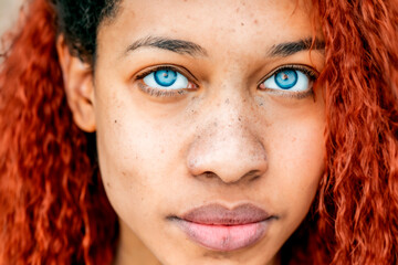 Close up afro portrait of black teenage girl with bright blue eyes, freckles and hair dyed red