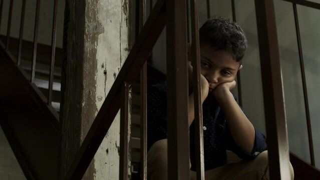 Portrait of a sad boy sitting on a dark staircase