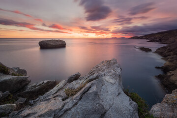 Warm sunrise in Islares, Cantabria, with a close-up of rocks and a rock in the middle of the sea