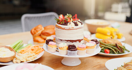 Birthday cake, table and food for event, celebration and party on patio with lunch meal. Dessert, home and outdoor with feast, vegetable and sweet baking with cupcake and sugar snack on a plate