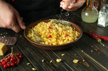 The chef adds salt to a plate of pasta. Working environment on the saloon kitchen table. Delicious pasta with vegetables for lunch