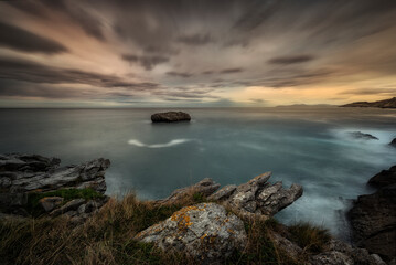 Sunset in Cotonera cove in Islares, Cantabria with a cloudy sky and warm colors and the rock...