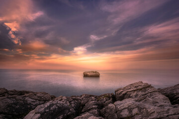 Sunset in Cotonera cove in Islares, Cantabria with a cloudy sky and warm colors and the rock...