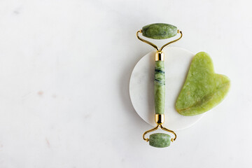 Green jade roller massager for face on white marble.