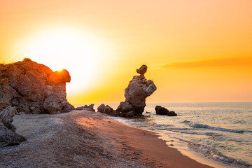 Sunset landscape. A fancy stone rock in the shape of a rooster on the seashore during sunset....