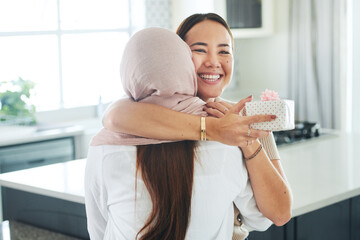 Birthday, gift and smile with friends hugging in kitchen of home together for celebration or surprise. Box, present and wow with happy young women embracing in apartment for anniversary milestone