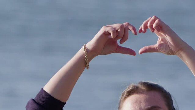 young girl making a heart sign with her hand on the beach