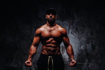Young strong man bodybuilder in cap on stone wall background - obrazy, fototapety, plakaty