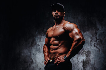 Fototapeta premium Young strong man bodybuilder in cap on stone wall background