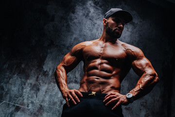 Young strong man bodybuilder in cap on stone wall background