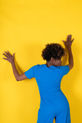 A woman in a blue outfit is leaning against a yellow wall