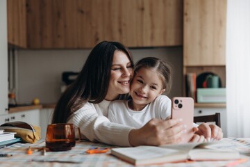 happy mother and daughter taking photo on phone at home at kitchen table