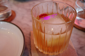 Close-up of a cold cocktail with a large ice cube, served in a faceted glass that catches the...