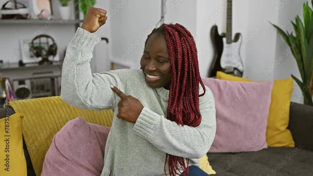 Canvas Prints Happy woman with braids flexing arm muscles in a cozy living room.