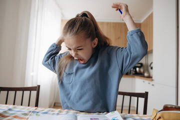 emotionally excited and angry first grader doing homework at home at the kitchen table