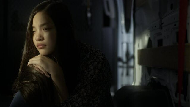 Young abused girl looks off into the distance while sitting in a dark car