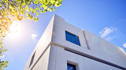 Modern white concrete building walls against blue sky. Eco architecture. Green trees and concrete office building. The harmony of nature and modernity. - obrazy, fototapety, plakaty