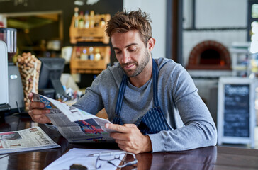 Small business, cafe and man at table with newspaper, paperwork and relax in coffee shop. Reading,...