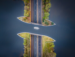 A boat sails through the aquaduct on the lake above the highway. Drone top down view. Unusual look. 