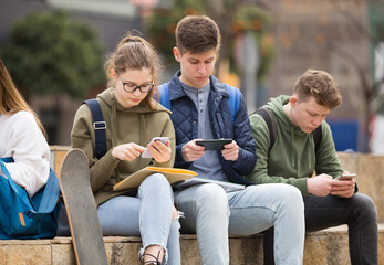 Four teenagers enthusiastically look at the screens of their smartphones on city street