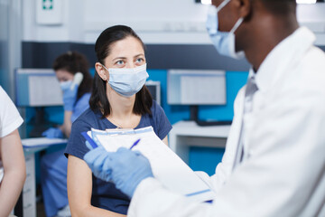 Close-up of a doctor in a lab coat and face mask talking to a caucasian woman in a medical office....