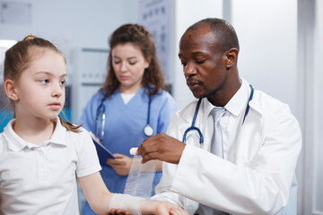 Close-up of a patient arm injury being methodically wrapped in sterile bandage by multicultural medical workers. Young child is being treated by a doctor and a nurse in this photograph.