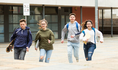 Fototapeta premium Group of cheerful glad students running outdoors in city street on good weather