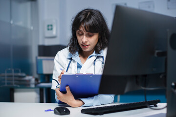 Close-up shot of female practitioner writing medical notes on her clipboard. Detailed image of a caucasian doctor dedicatedly reviewing information from patient consultations.