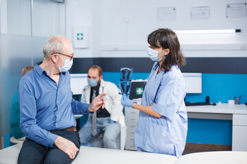 Nurse practitioner grasping ct scan results at medical consultation with elderly man during coronavirus pandemic. Healthcare specialist explains radiography diagnosis, finding lungs treatment.