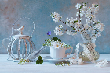 Spring floral still life. Blooming cherry plum branches in a vase, a cup and a teapot on a white wooden table. - 787549863