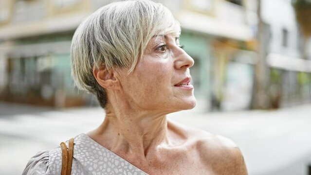Elegant senior hispanic woman with short grey hair gazing upward on a busy urban street.