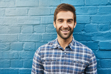 Man, smile in portrait and relax against wall background, casual fashion and positivity with blue...